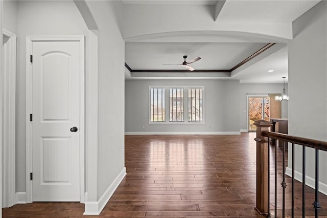 corridor featuring baseboards, a tray ceiling, an upstairs landing, hardwood / wood-style flooring, and arched walkways