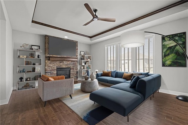 living room featuring a raised ceiling, a stone fireplace, hardwood / wood-style floors, and a ceiling fan