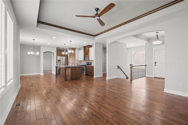 unfurnished living room featuring visible vents, a raised ceiling, dark wood-style floors, and ceiling fan with notable chandelier