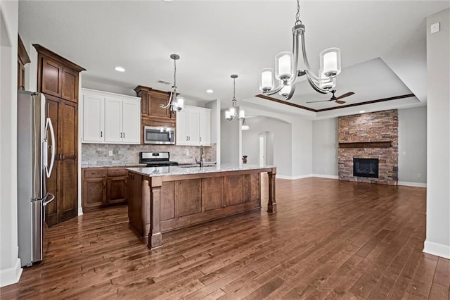 kitchen featuring dark wood-style floors, a tray ceiling, appliances with stainless steel finishes, ceiling fan with notable chandelier, and backsplash