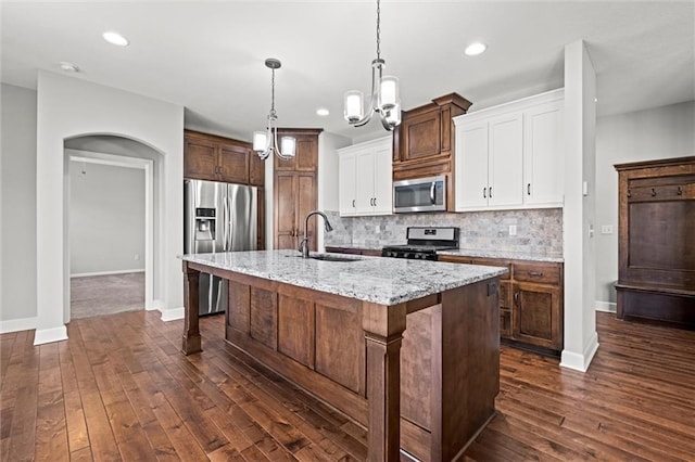 kitchen with dark wood finished floors, an island with sink, a sink, appliances with stainless steel finishes, and backsplash