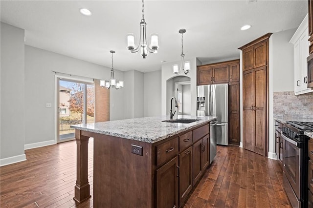 kitchen featuring light stone counters, a sink, decorative backsplash, appliances with stainless steel finishes, and a chandelier