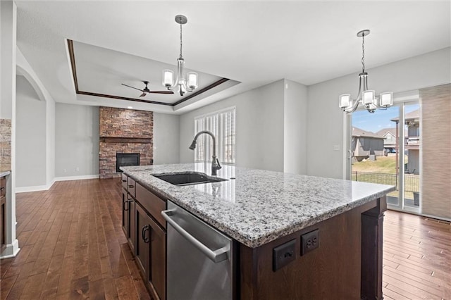 kitchen with a fireplace, a sink, dishwasher, a raised ceiling, and ceiling fan with notable chandelier