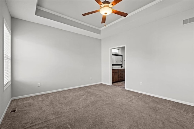 carpeted spare room featuring a raised ceiling, a healthy amount of sunlight, and visible vents