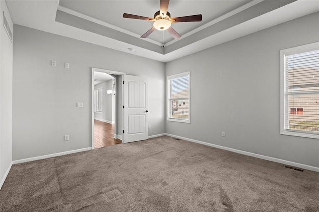 carpeted empty room with baseboards, a raised ceiling, visible vents, and ceiling fan