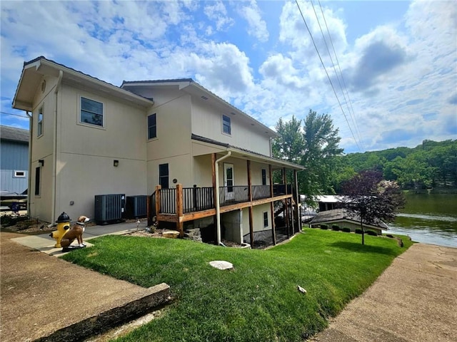 rear view of house with a deck with water view, a yard, and central AC