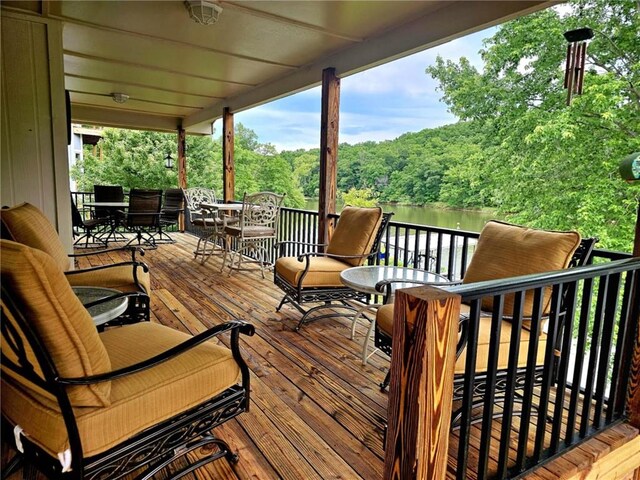 wooden deck featuring outdoor dining space, a water view, and a wooded view