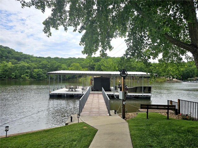 dock area with a water view, a lawn, boat lift, and a wooded view