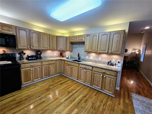 kitchen featuring tasteful backsplash, brown cabinetry, dark wood-type flooring, black appliances, and a sink