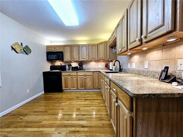 kitchen with tasteful backsplash, a sink, black appliances, light wood-type flooring, and baseboards