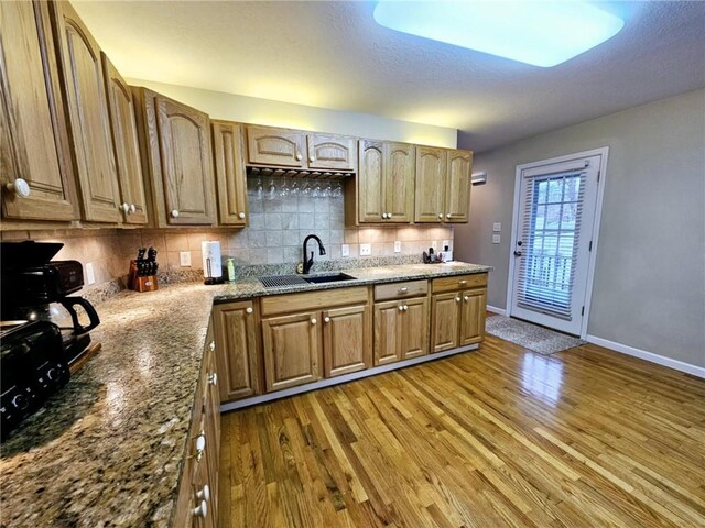 kitchen with baseboards, light stone counters, wood finished floors, a sink, and backsplash