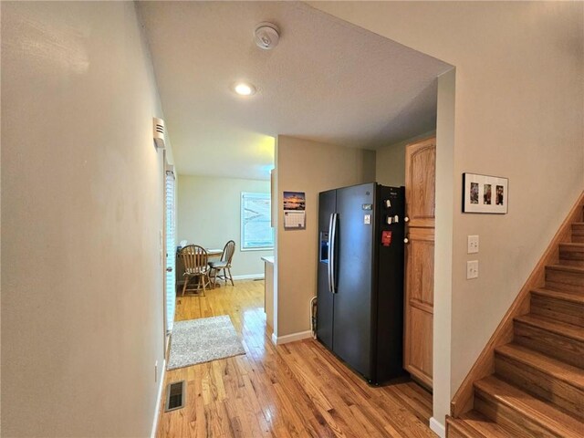 hall with light wood-style floors, visible vents, baseboards, and stairs