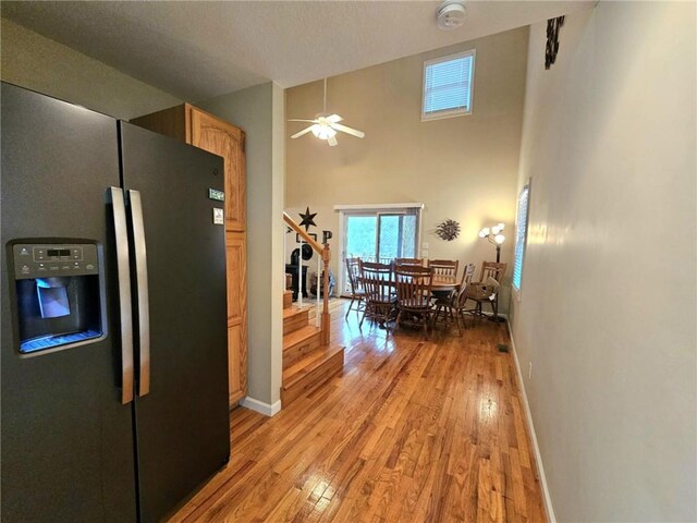 kitchen featuring stainless steel fridge, baseboards, a high ceiling, light brown cabinetry, and light wood-style floors