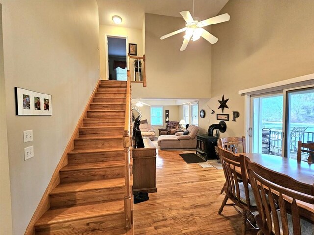 stairs featuring baseboards, ceiling fan, wood finished floors, a wood stove, and a high ceiling