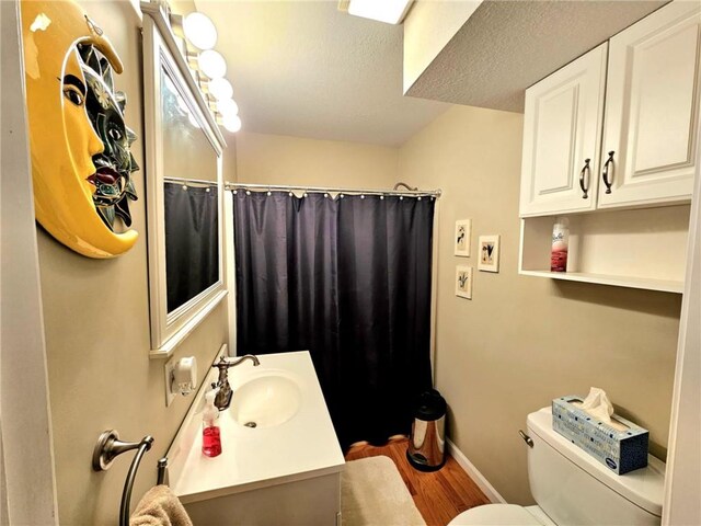 full bathroom featuring a textured ceiling, toilet, wood finished floors, vanity, and baseboards