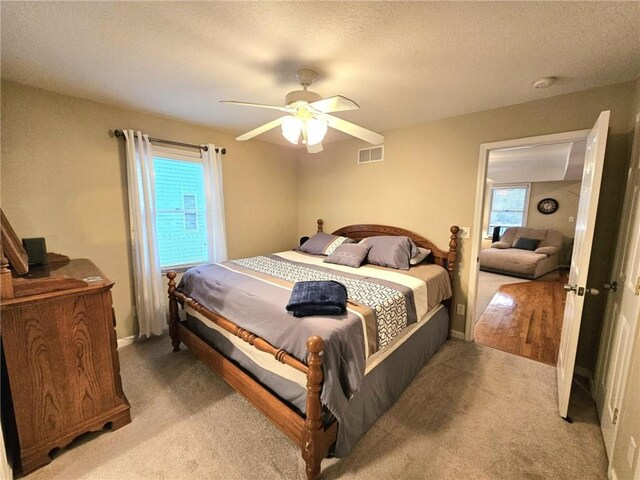 bedroom featuring light carpet, a textured ceiling, visible vents, and a ceiling fan