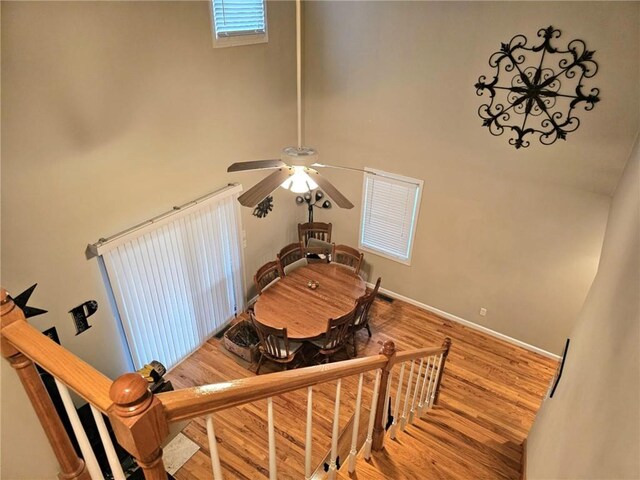 staircase with ceiling fan, a high ceiling, wood finished floors, and baseboards