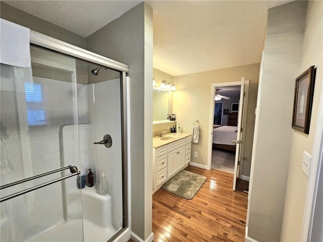 full bathroom featuring wood finished floors, vanity, baseboards, a stall shower, and ensuite bath