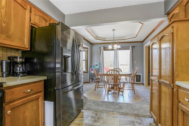 kitchen with a chandelier, black fridge with ice dispenser, brown cabinets, and a tray ceiling