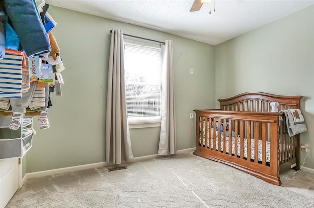 bedroom with baseboards, a nursery area, and carpet flooring