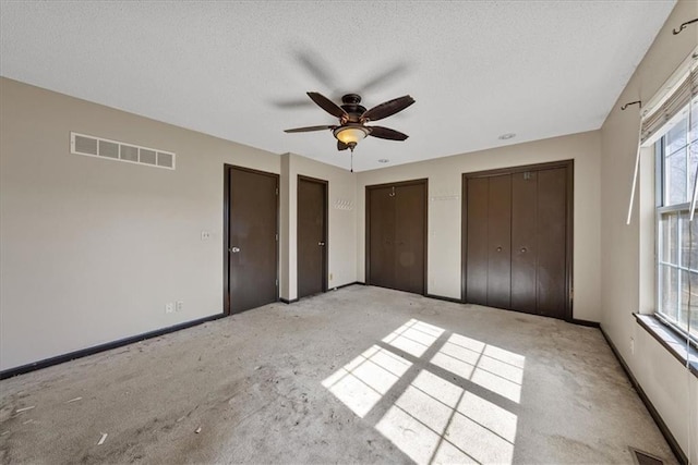 unfurnished bedroom featuring baseboards, a textured ceiling, visible vents, and two closets