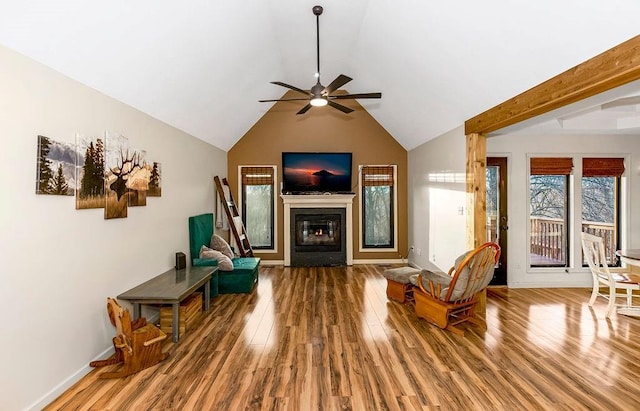 living area with a ceiling fan, a glass covered fireplace, vaulted ceiling, wood finished floors, and baseboards