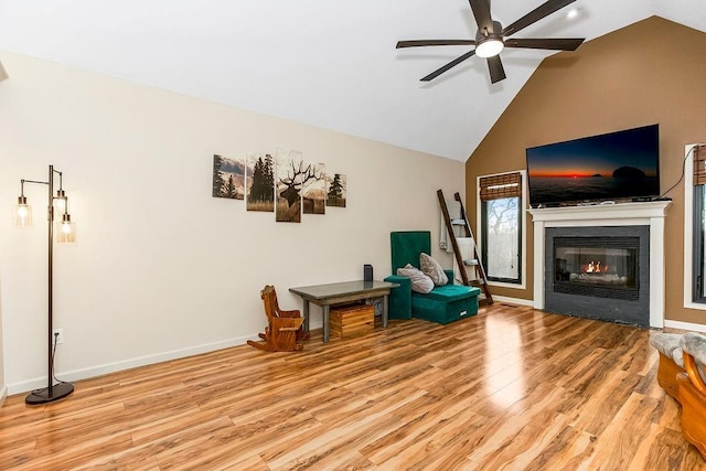 sitting room with a ceiling fan, a glass covered fireplace, baseboards, and light wood finished floors