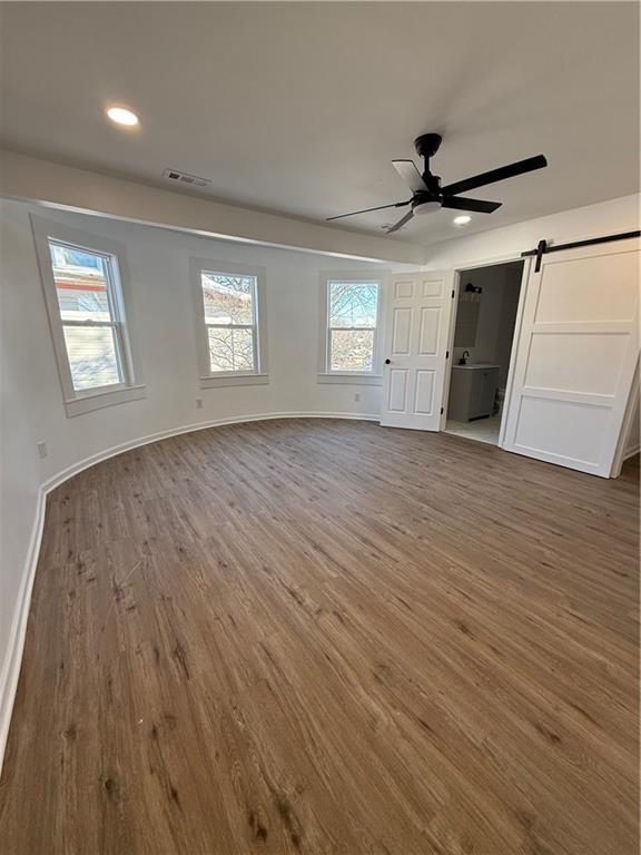 unfurnished bedroom featuring a barn door, visible vents, baseboards, wood finished floors, and recessed lighting