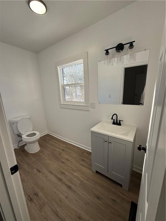 half bathroom with toilet, baseboards, wood finished floors, and vanity