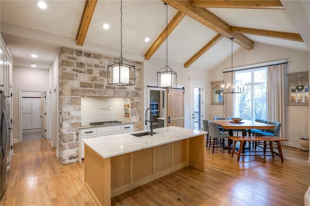 kitchen featuring light stone counters, a sink, white cabinetry, an island with sink, and pendant lighting