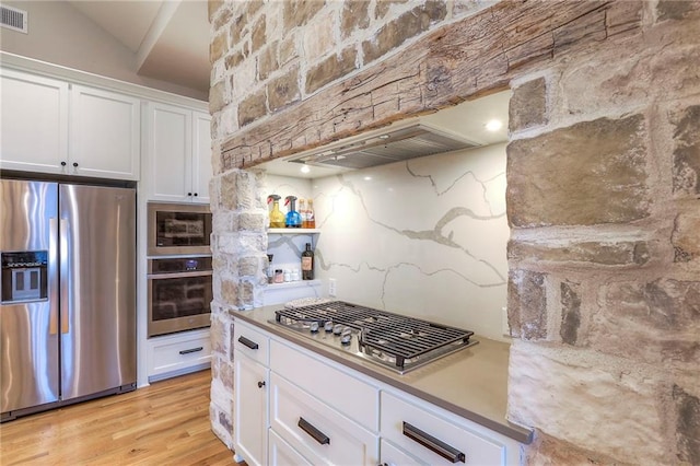 kitchen featuring stainless steel appliances, tasteful backsplash, light countertops, light wood-style floors, and white cabinetry