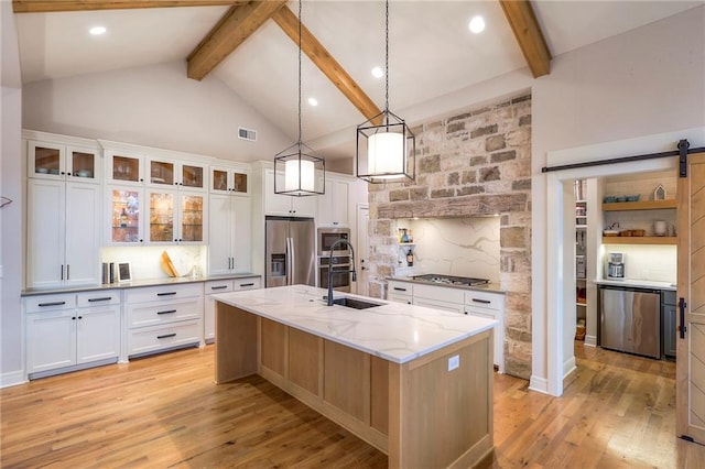 kitchen featuring white cabinets, an island with sink, glass insert cabinets, stainless steel appliances, and a sink