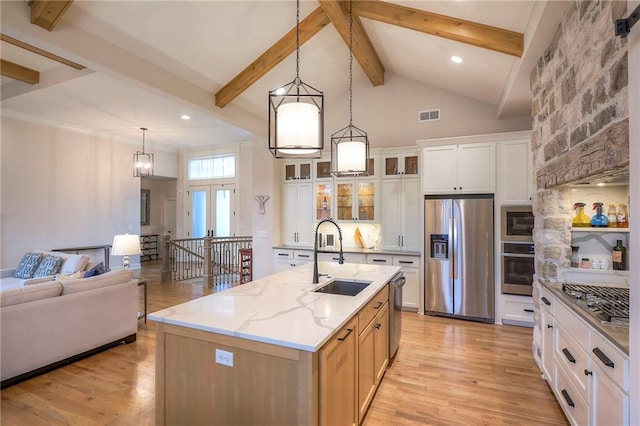 kitchen with stainless steel appliances, white cabinetry, a center island with sink, light stone countertops, and glass insert cabinets