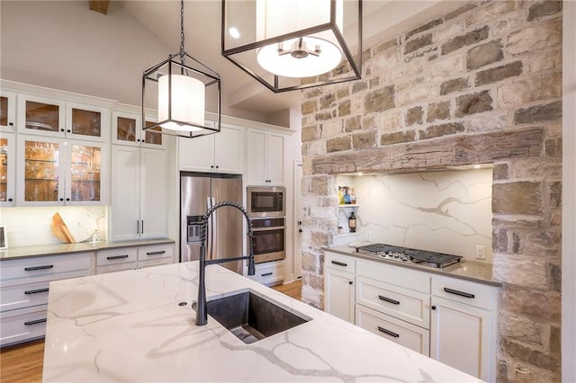 kitchen with light stone counters, decorative light fixtures, stainless steel appliances, white cabinetry, and a sink