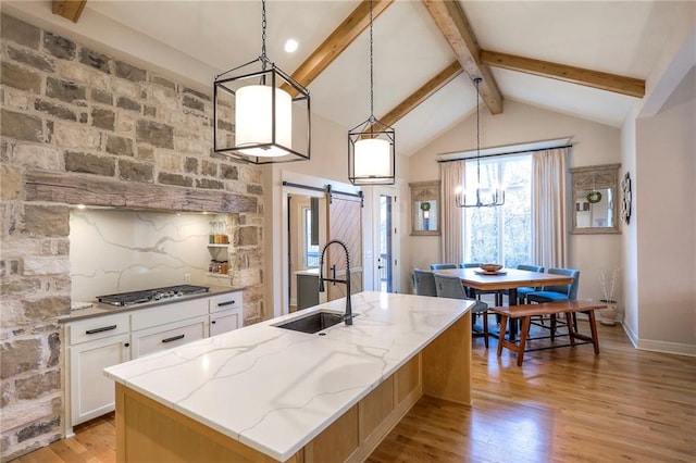 kitchen featuring a barn door, a center island with sink, light stone counters, white cabinetry, and pendant lighting