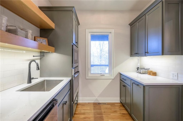 kitchen featuring light wood-style flooring, a sink, baseboards, backsplash, and open shelves