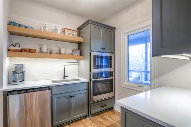 kitchen featuring stainless steel appliances, light countertops, a sink, and open shelves