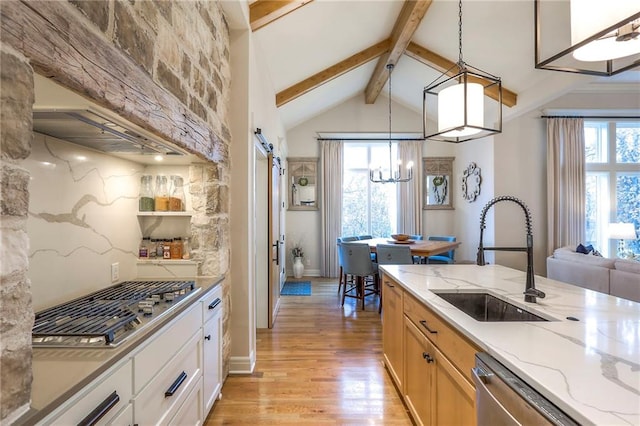 kitchen with a barn door, a sink, appliances with stainless steel finishes, light stone countertops, and pendant lighting