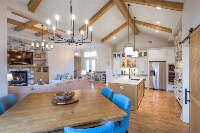 dining area featuring a barn door, beamed ceiling, light wood-type flooring, a fireplace, and high vaulted ceiling