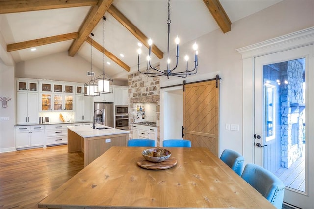 dining area featuring high vaulted ceiling, a barn door, beamed ceiling, and light wood-type flooring