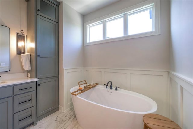 full bath featuring a freestanding bath, marble finish floor, wainscoting, and vanity