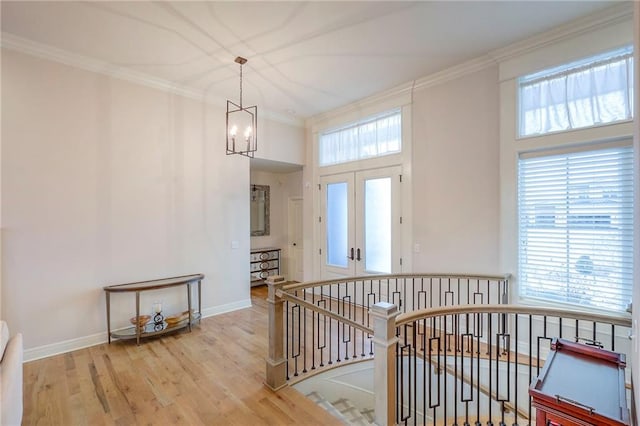 hall featuring ornamental molding, a chandelier, light wood finished floors, and an upstairs landing