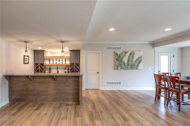 interior space featuring a dry bar, visible vents, wood finished floors, and decorative light fixtures