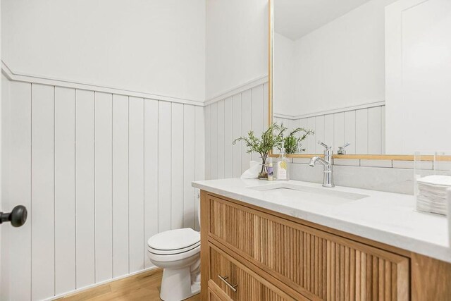 half bathroom featuring a wainscoted wall, toilet, wood finished floors, and vanity
