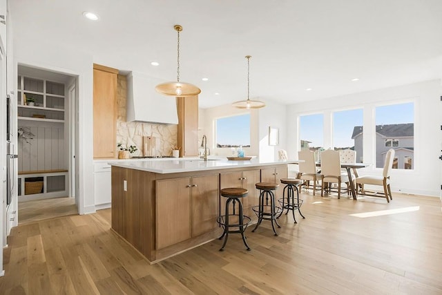 kitchen featuring a center island with sink, light countertops, custom range hood, a wealth of natural light, and light wood-style flooring