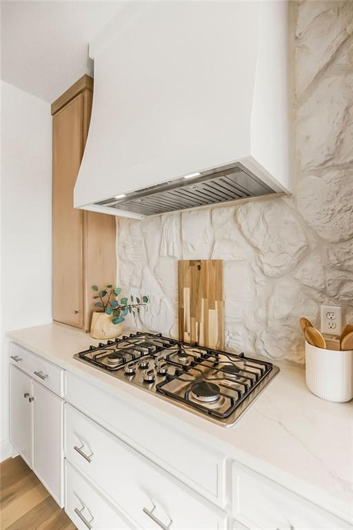 kitchen featuring stainless steel gas cooktop, decorative backsplash, white cabinetry, and custom exhaust hood