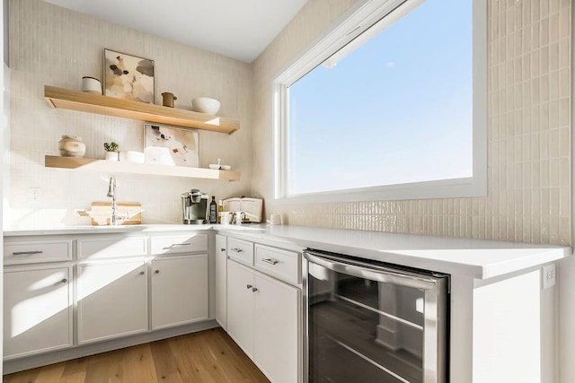 kitchen with light wood-style flooring, open shelves, wine cooler, light countertops, and decorative backsplash