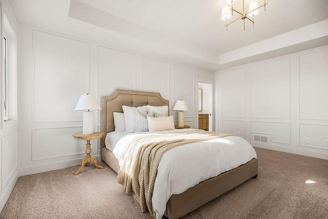 carpeted bedroom featuring a tray ceiling, an inviting chandelier, visible vents, and a decorative wall