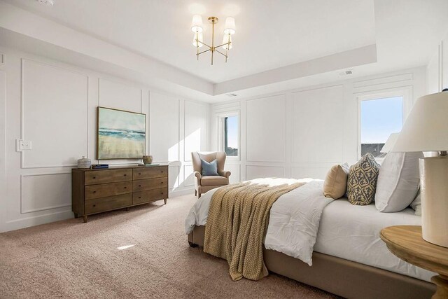 bedroom with multiple windows, a raised ceiling, light colored carpet, and a decorative wall