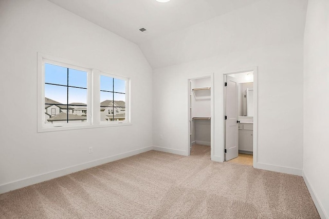 unfurnished bedroom with baseboards, lofted ceiling, a spacious closet, a closet, and light colored carpet